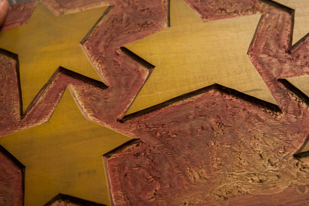 Eine Nahaufnahme von drei gelben Sternen, die in eine strukturierte, rötlich-braune Holzoberfläche geschnitzt sind.