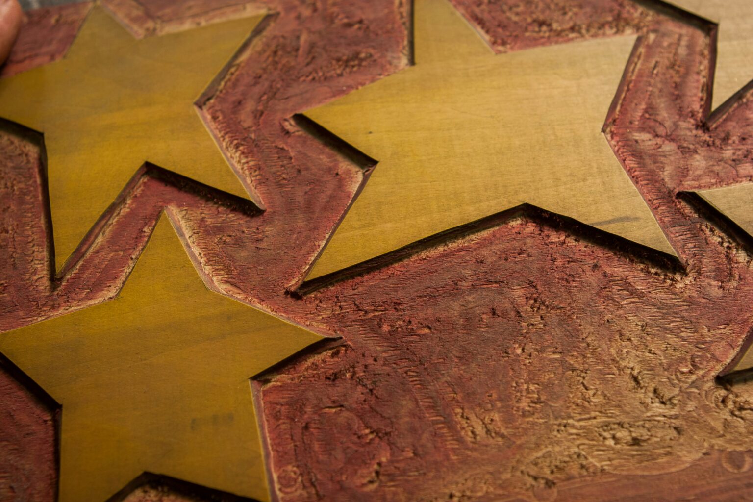 Eine Nahaufnahme von drei gelben Sternen, die in eine strukturierte, rötlich-braune Holzoberfläche geschnitzt sind.