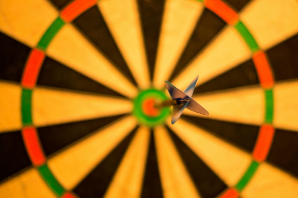 Ein Dartpfeil trifft perfekt das Bullseye auf einer Dartscheibe, von oben gesehen mit dem Dartpfeil und der Mitte der Scheibe im scharfen Fokus.