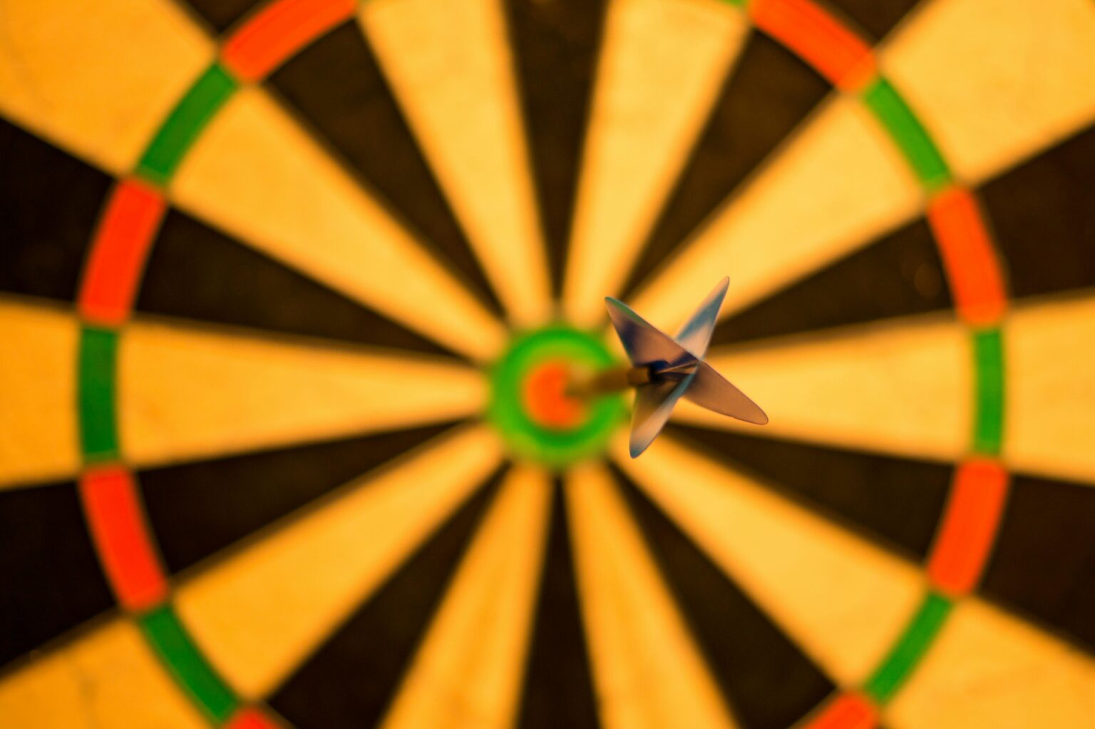 Ein Dartpfeil trifft perfekt das Bullseye auf einer Dartscheibe, von oben gesehen mit dem Dartpfeil und der Mitte der Scheibe im scharfen Fokus.