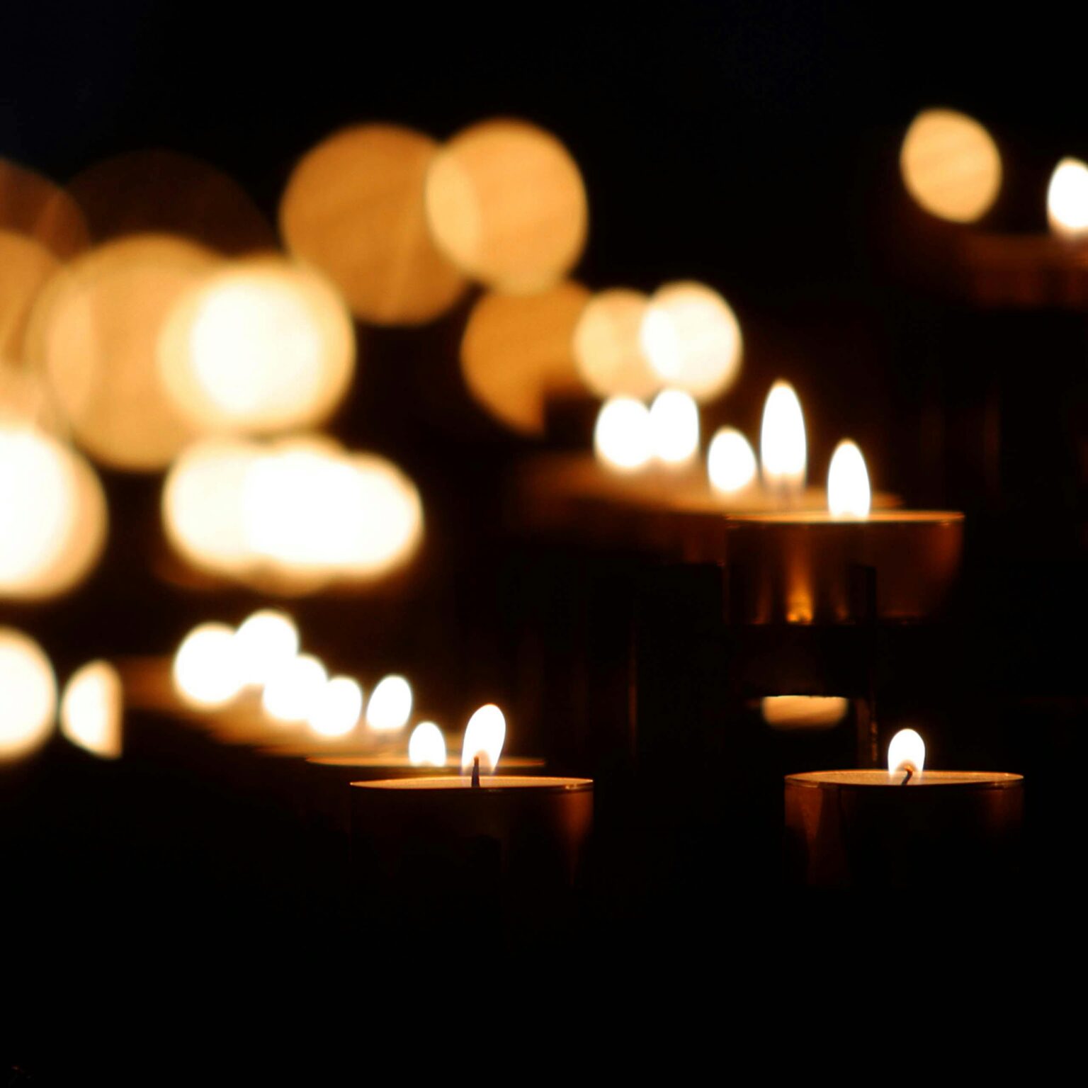 Mehrere brennende Kerzen leuchten warm in der Dunkelheit, während im Hintergrund sanfte, verschwommene Lichter eine friedliche, ruhige Atmosphäre schaffen.