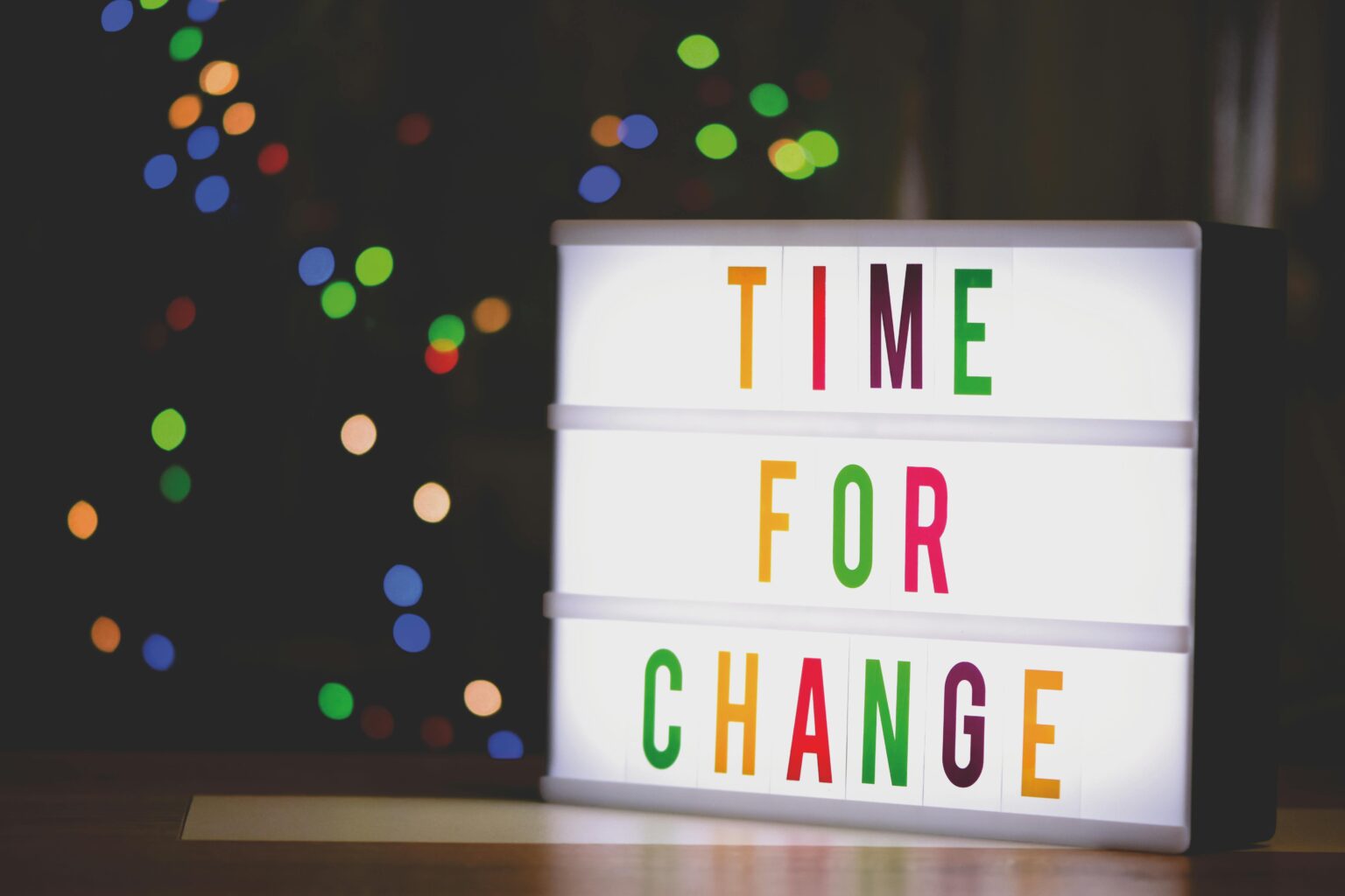 Ein Leuchtkasten zeigt die Worte TIME FOR CHANGE in bunten Buchstaben, mit verschwommenen bunten Lichtern im Hintergrund.