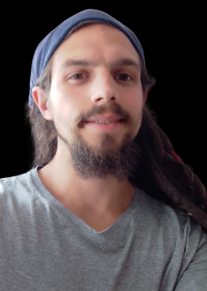 Ein lächelnder Mann mit Bart, der ein blaues Kopftuch und ein graues Hemd trägt, steht vor einem schwarzen Hintergrund.